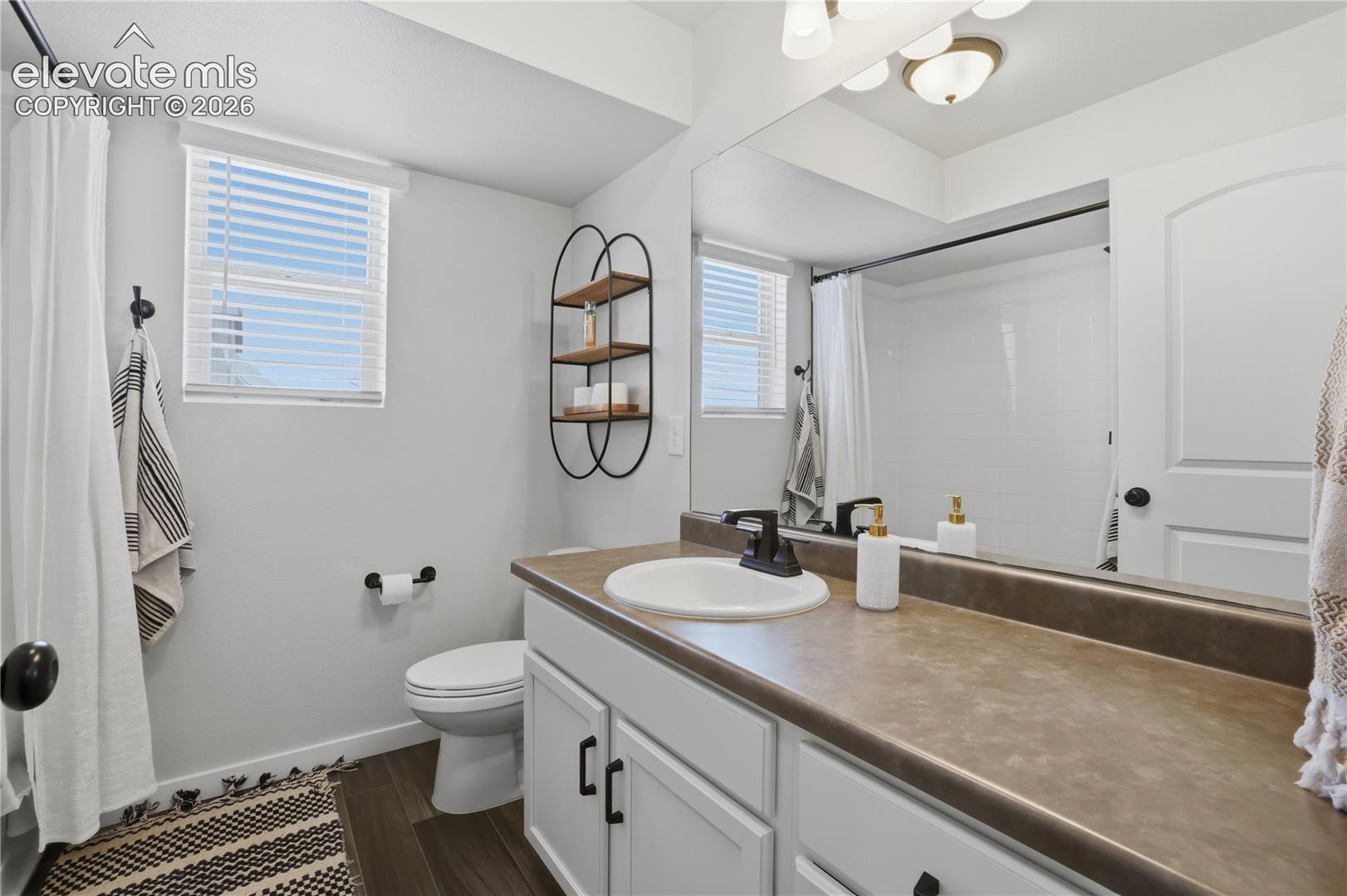6008 Ashmore Road Colorado Springs, CO 80927 - Photo 28 of 48 Full bathroom featuring a single vanity with a white basin and dark countertop, white cabinetry with dark hardware, a large mirror, and a shower-tub combination with white subway tile surround
