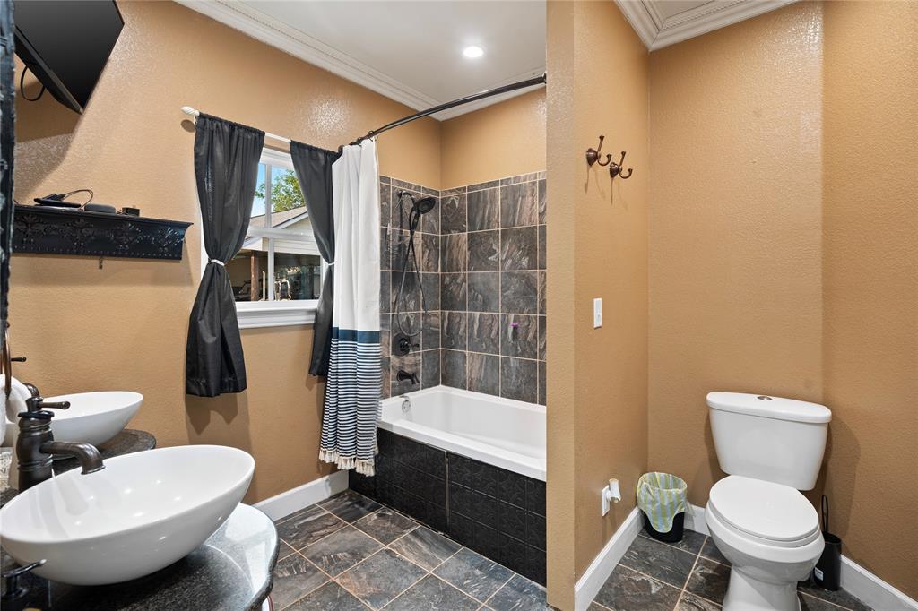 202 North Kickapoo Street Lipan, TX 76462 - Photo 19 of 38 Dual vessel sinks with dark bronze fixtures, integrated bathtub and shower with tile surround, toilet, and tiled flooring