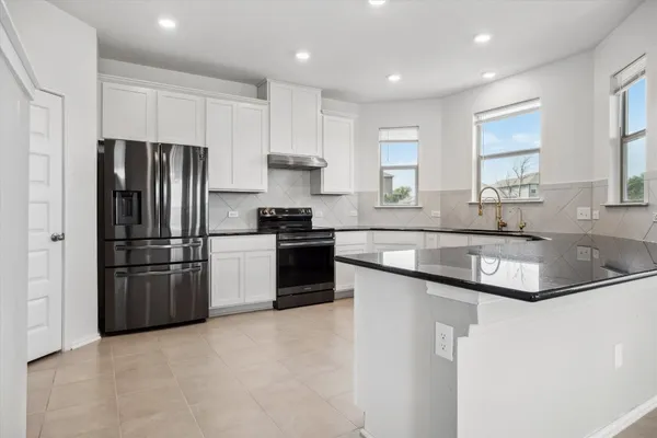 a kitchen with granite countertop white cabinets white appliances a sink and a large window