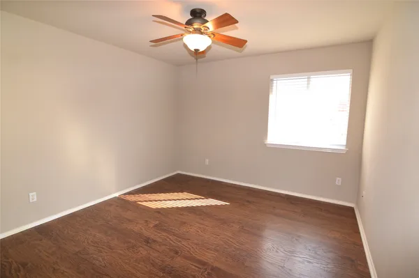 an empty room with wooden floor chandelier fan and windows