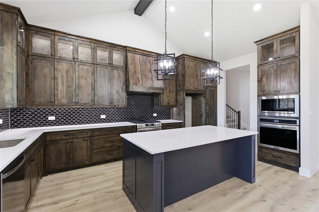 713 Anne Road Van Alstyne, TX 75495 - Photo 7 of 29 Kitchen featuring a central island, dark wood-finish cabinetry, light wood-finish flooring, a herringbone mosaic tile backsplash, and stainless steel appliances
