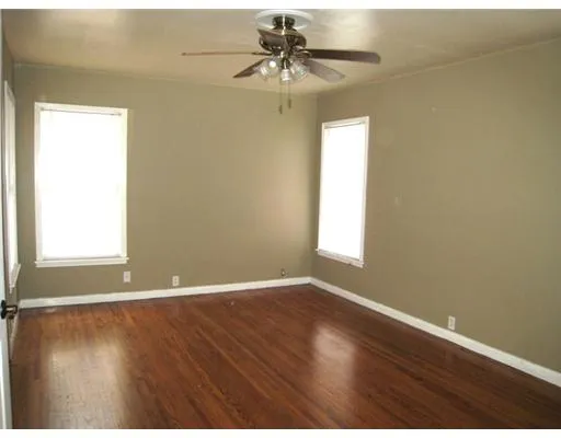 an empty room with wooden floor chandelier fan and windows