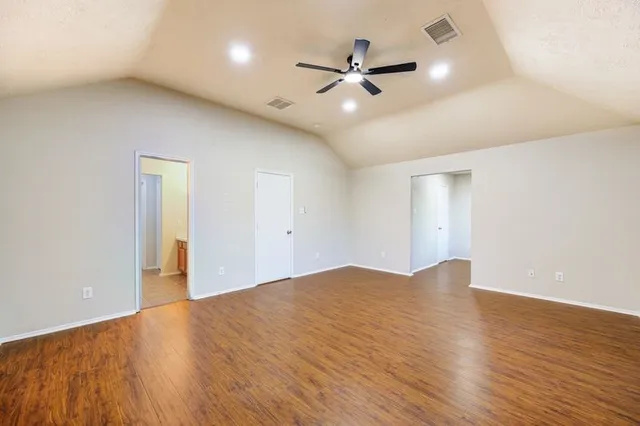 a view of an empty room with wooden floor and a ceiling fan