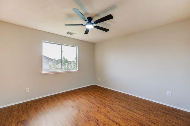 an empty room with wooden floor ceiling fan and windows