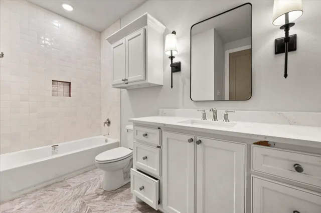 a bathroom with a toilet a sink a mirror a bathtub and vanity