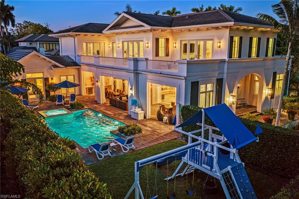 215 3rd Avenue North Naples, FL 34102 - Photo 44 of 47 Back of house at dusk featuring a balcony, a patio, stucco siding, a tile roof, and a pool with connected hot tub