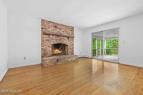 a view of an empty room with wooden floor fireplace and a window