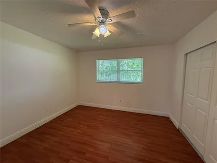 an empty room with wooden floor chandelier fan and windows