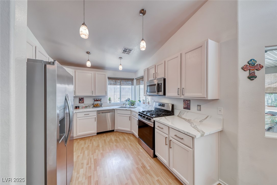 990 Ridge Path Avenue Henderson, NV 89015 - Photo 12 of 41 Kitchen with stainless steel appliances, light wood-style flooring, white cabinets, light stone countertops, and vaulted ceiling