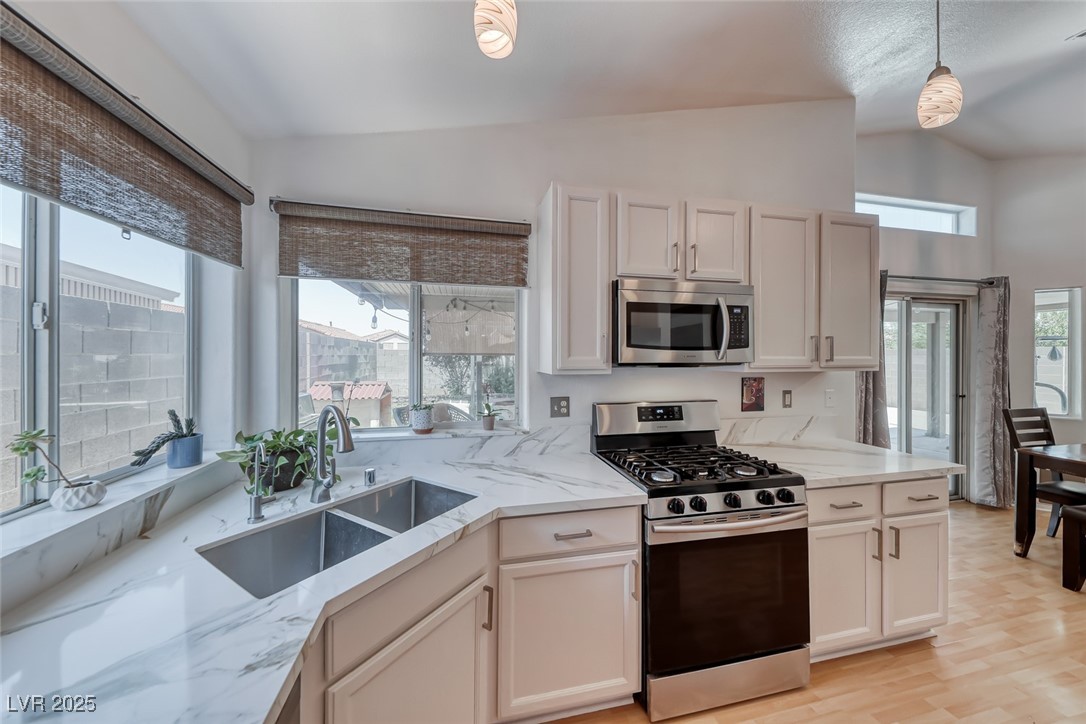 990 Ridge Path Avenue Henderson, NV 89015 - Photo 13 of 41 Kitchen with stainless steel appliances, vaulted ceiling, light stone counters, hanging light fixtures, and light wood-type flooring
