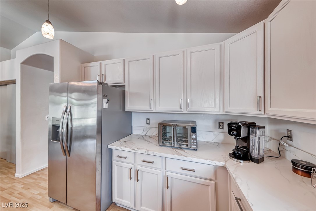 990 Ridge Path Avenue Henderson, NV 89015 - Photo 14 of 41 Kitchen with lofted ceiling, stainless steel refrigerator with ice dispenser, light stone countertops, hanging light fixtures, and white cabinets