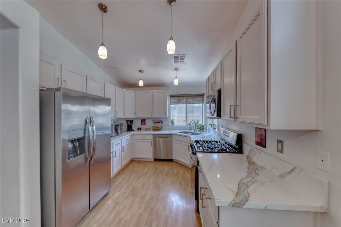 990 Ridge Path Avenue Henderson, NV 89015 - Photo 4 of 41 Kitchen featuring stainless steel appliances, vaulted ceiling, light wood finished floors, white cabinetry, and decorative light fixtures