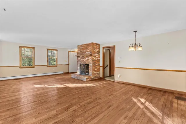 an empty room with wooden floor fireplace and windows