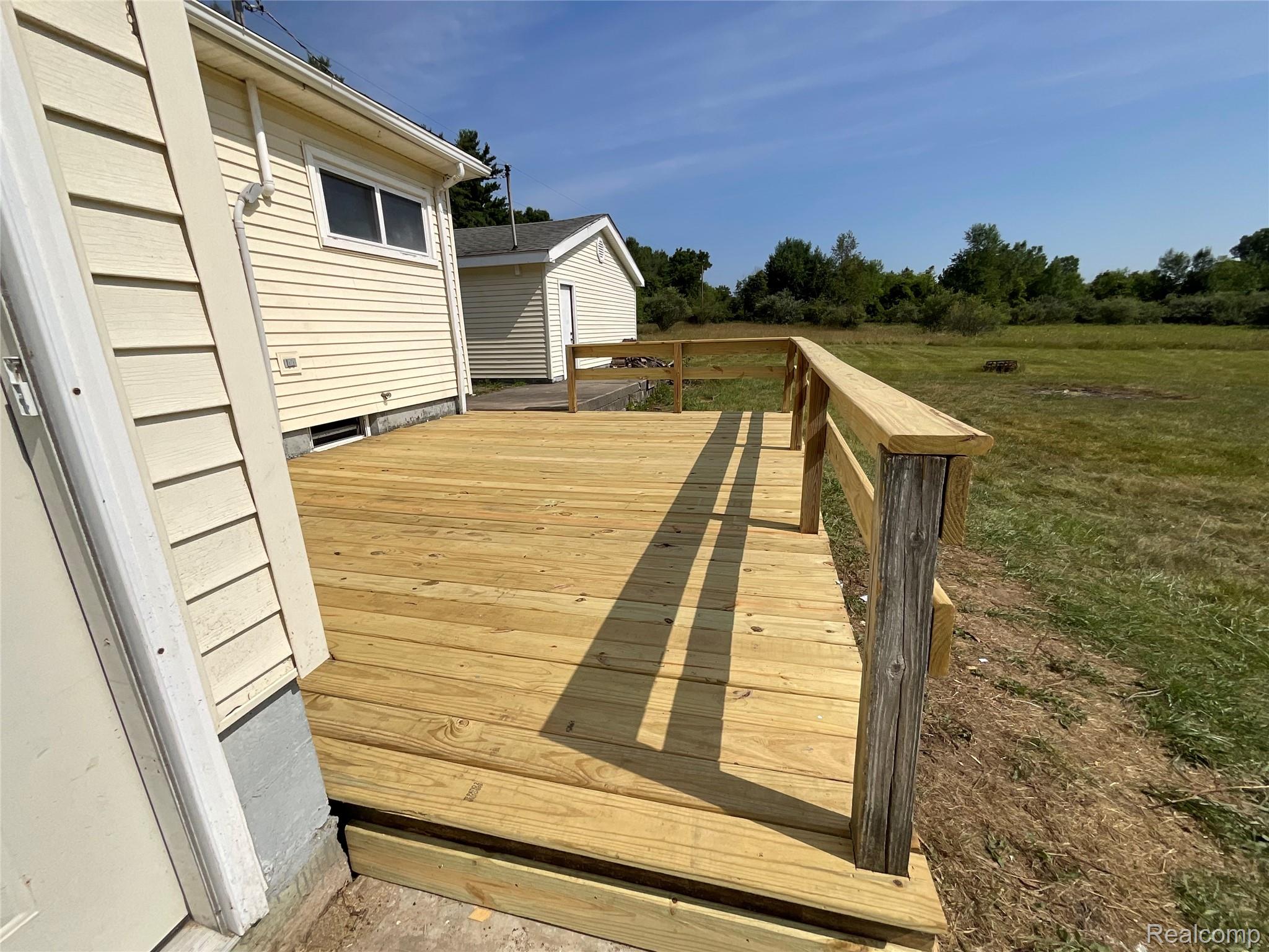 10119 Godfrey Road Bancroft, MI 48414 - Photo 7 of 47 Expansive wood deck with a perimeter railing, situated alongside horizontal siding, and bordered by a large grassy area
