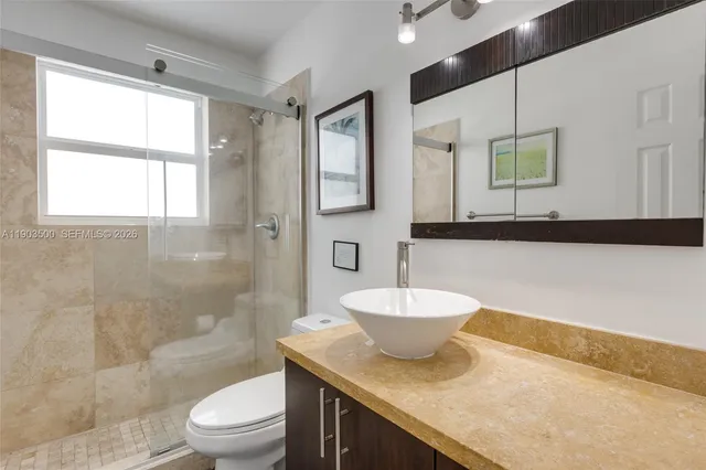 a bathroom with a granite countertop sink a toilet a mirror and shower