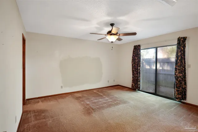 an empty room with chandelier fan and windows