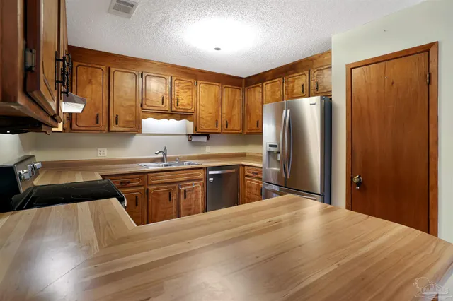 a kitchen with stainless steel appliances granite countertop a refrigerator a sink dishwasher a stove with wooden cabinets and floor