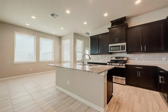 a large kitchen with kitchen island granite countertop a stove top oven a sink a counter space and cabinets