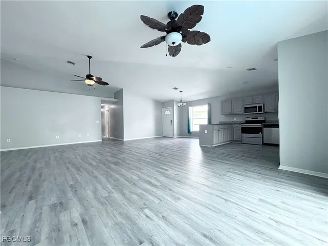 a view of an empty room and kitchen with wooden floor