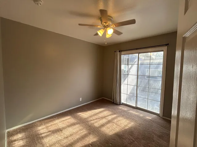 an empty room with chandelier fan and windows