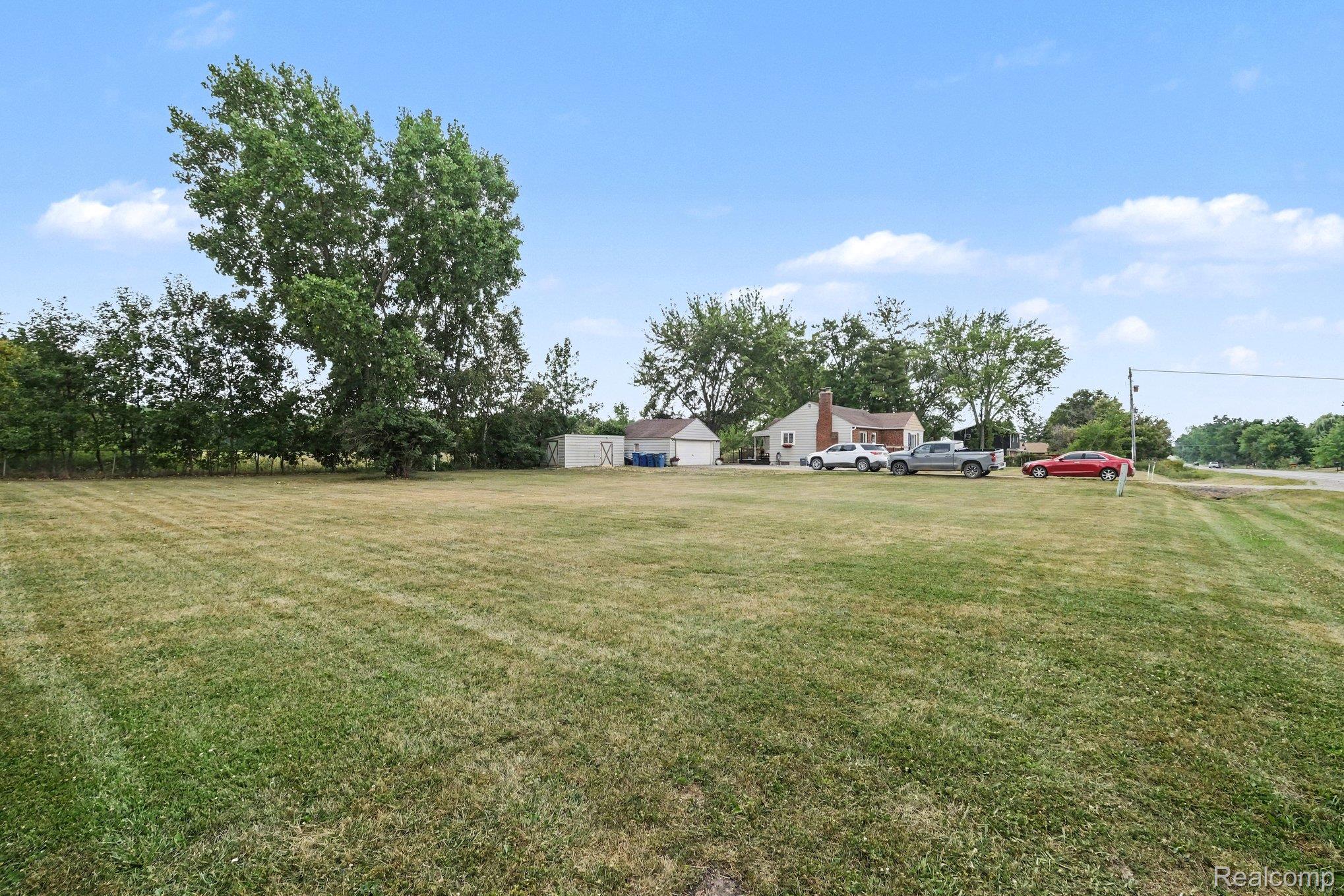 5409 Baldwin Road Swartz Creek, MI 48473 - Photo 20 of 27 Expansive green lawn with a detached shed, mature trees, and a distant single-story dwelling with a brick chimney