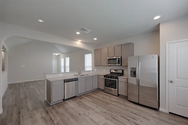 a kitchen with stainless steel appliances granite countertop white cabinets a refrigerator a sink a stove a microwave and wooden floors