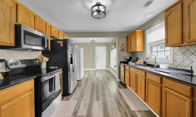 a kitchen with stainless steel appliances a stove top oven a sink dishwasher a microwave oven and a refrigerator with wooden floor