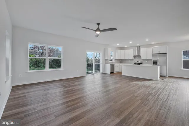 a view of an empty room with wooden floor and a ceiling fan