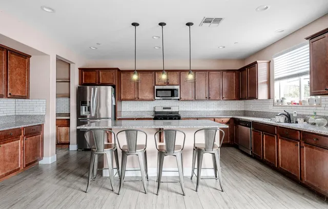 a kitchen with stainless steel appliances granite countertop a stove top oven a refrigerator a sink and chairs