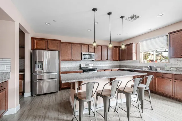 a kitchen with granite countertop stainless steel appliances a refrigerator a sink and wooden floors