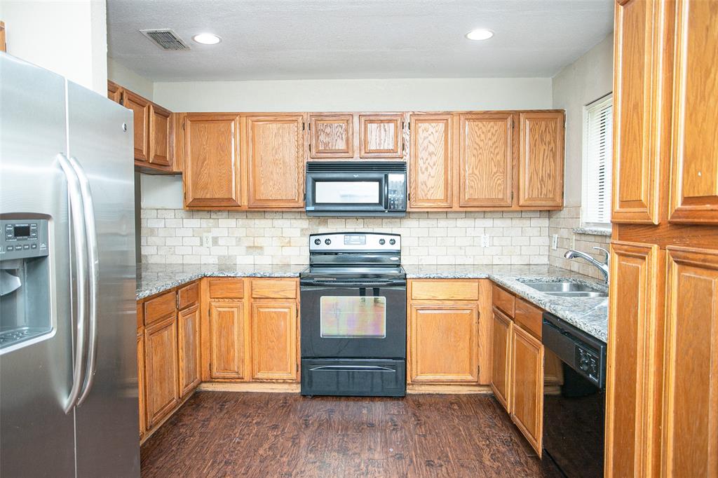 2019 West Nathan Lowe Road Arlington, TX 76017 - Photo 6 of 21 U-shaped kitchen featuring wood-finish cabinetry, granite-style countertops, subway tile backsplash, and wood-finish flooring