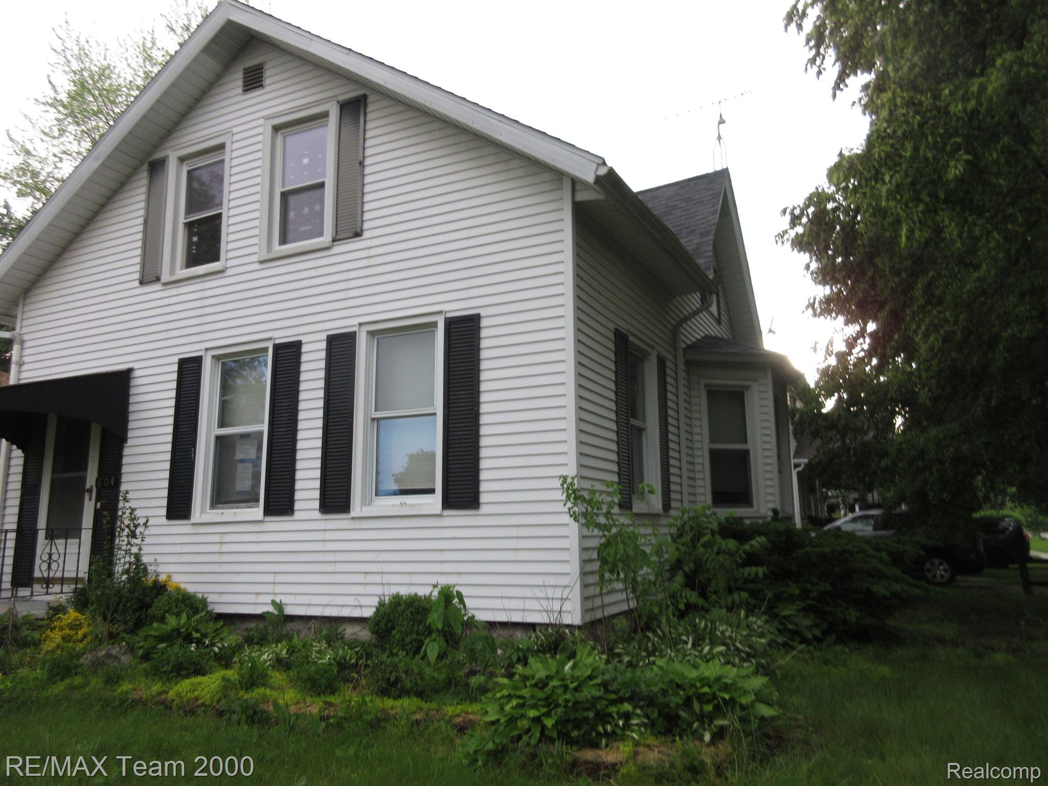 604 Smith Street Monroe, MI 48161 - Photo 2 of 24 White siding exterior with multiple windows, black shutters, and a covered entry with a black awning