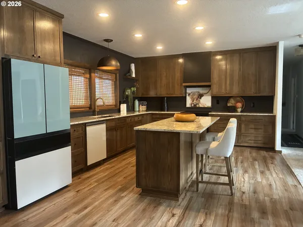 a kitchen with stainless steel appliances granite countertop wooden cabinets a refrigerator a sink a stove a microwave and island with wooden floor