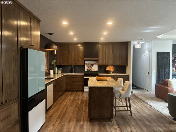 a kitchen with stainless steel appliances granite countertop a refrigerator a sink a stove a dining table and chairs with wooden floor