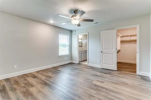 a view of an empty room with wooden floor and a ceiling fan