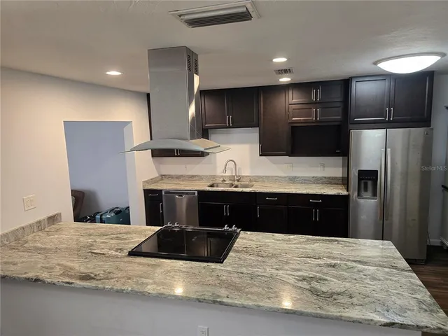 a kitchen with stainless steel appliances kitchen island granite countertop a refrigerator and a sink
