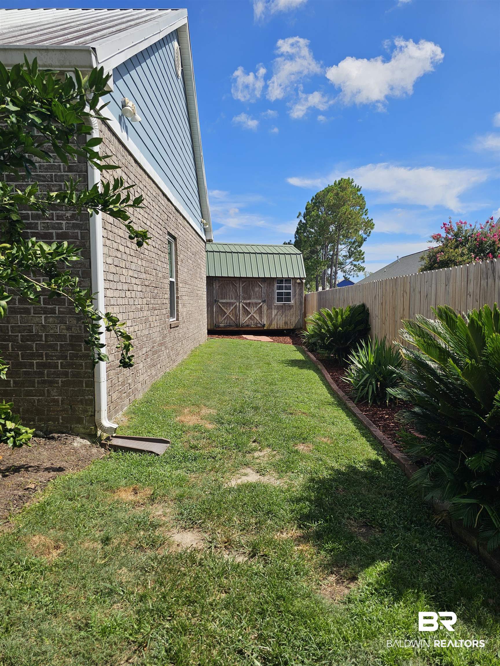 1181 Sloane Cove Foley, AL 36535 - Photo 5 of 10 Expansive side yard featuring a brick exterior, light blue siding, a storage shed with a green metal roof, a wooden privacy fence, and established landscaping