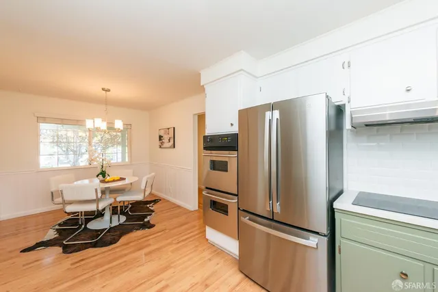 a kitchen with stainless steel appliances kitchen island granite countertop a refrigerator a oven a sink a dining table and chairs with wooden floor