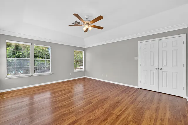 an empty room with wooden floor chandelier fan and windows