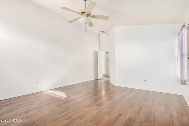 an empty room with wooden floor ceiling fan and window