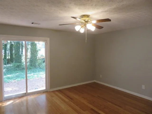 a view of an empty room with wooden floor and fan