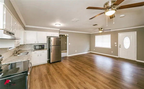 a kitchen with stainless steel appliances granite countertop a refrigerator a stove a sink and white cabinets with wooden floor