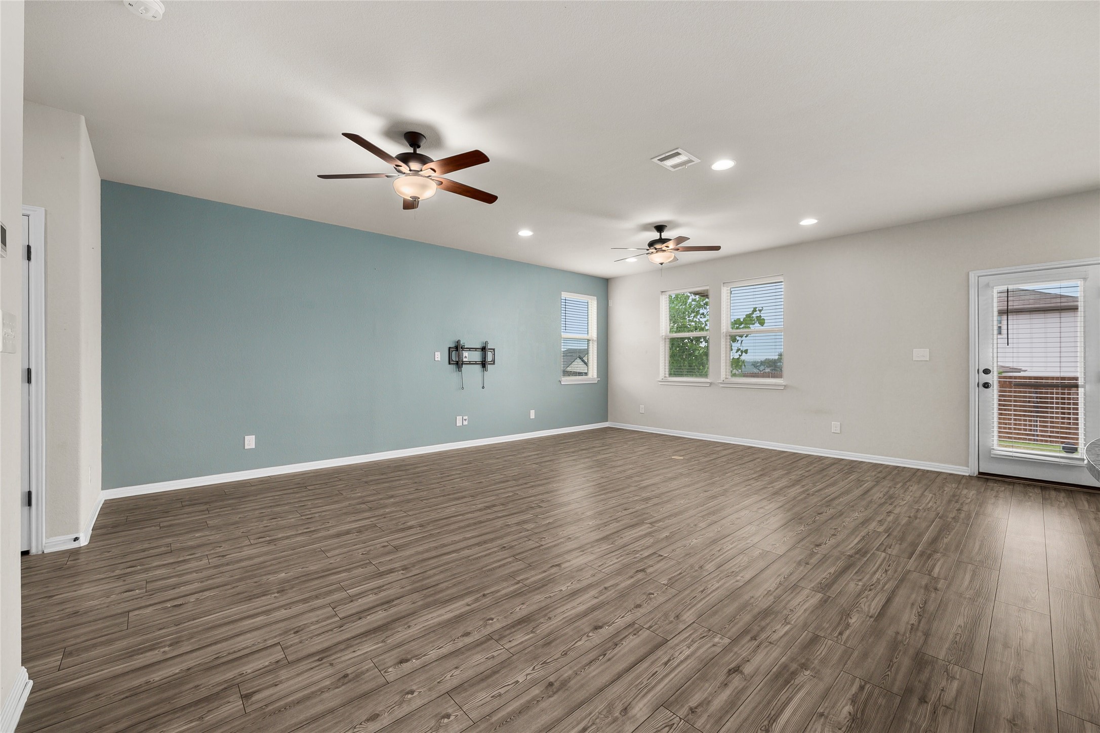 101 Lambert Street Leander, TX 78641 - Photo 7 of 33 A spacious common area boasts warm wood-look flooring, multiple windows, and dual ceiling fans for comfort.