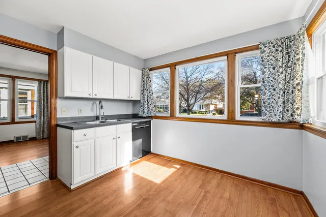 a kitchen with granite countertop a stove a sink and white cabinets with wooden floor next to windows