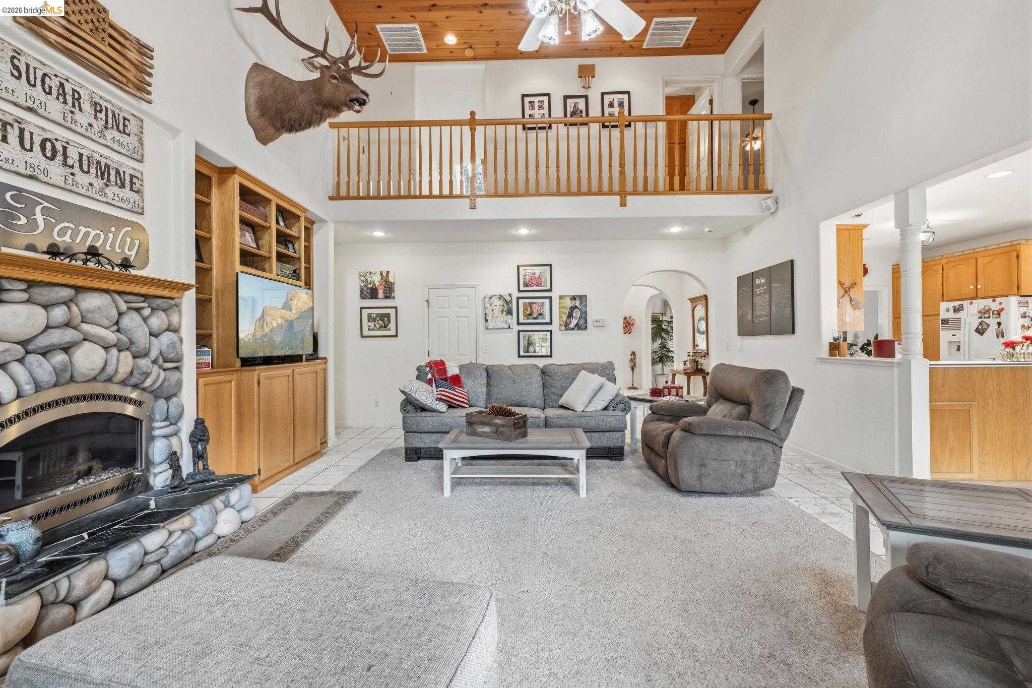 18450 Lambert Lake Road Sonora, CA 95370 - Photo 42 of 87 Two-story living area featuring a stone fireplace with hearth, a built-in entertainment center, a wood-finish ceiling, and an upper-level balcony with a wood railing