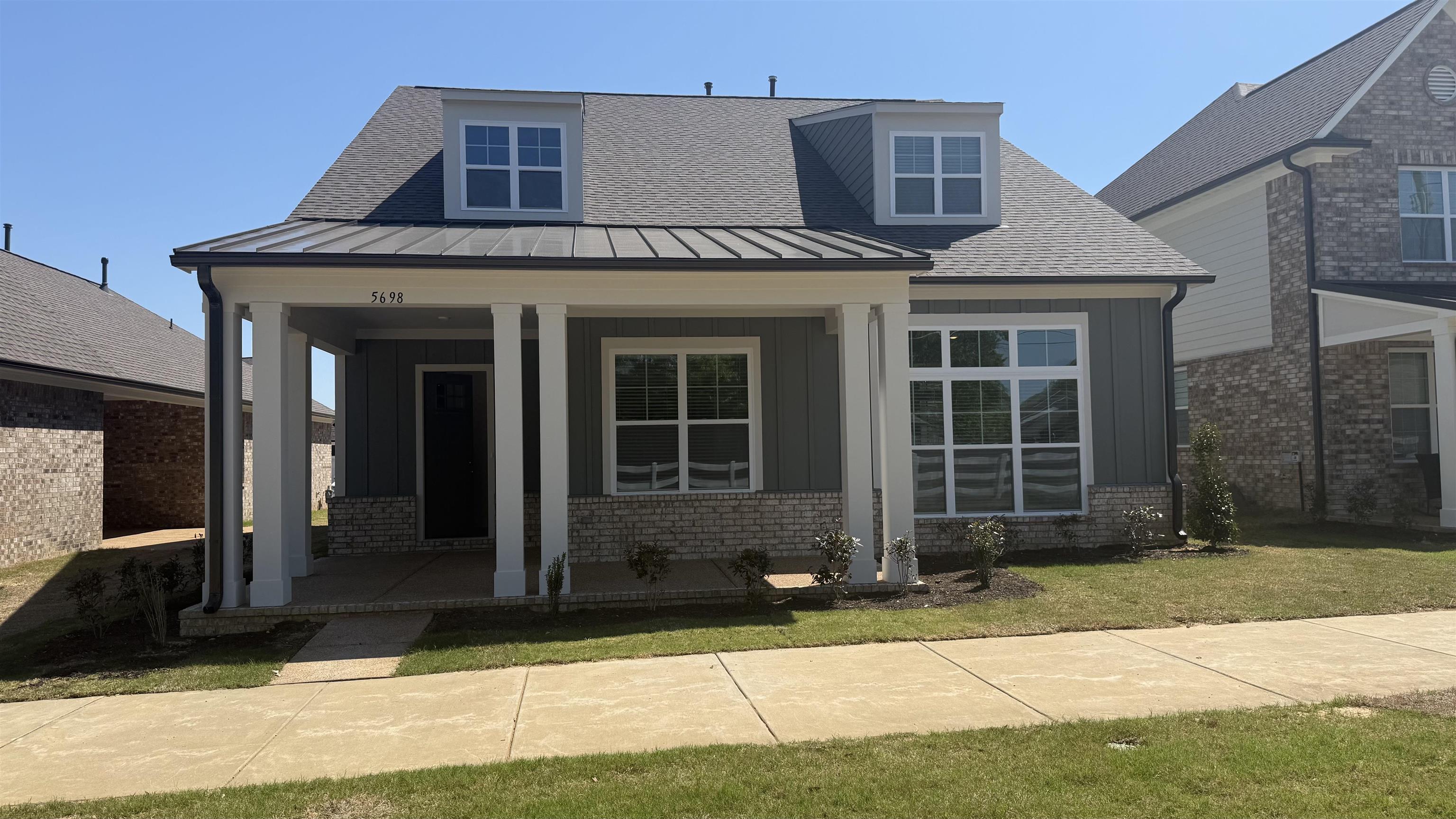 View of front of property with a porch, brick siding, a standing seam roof, and a front yard