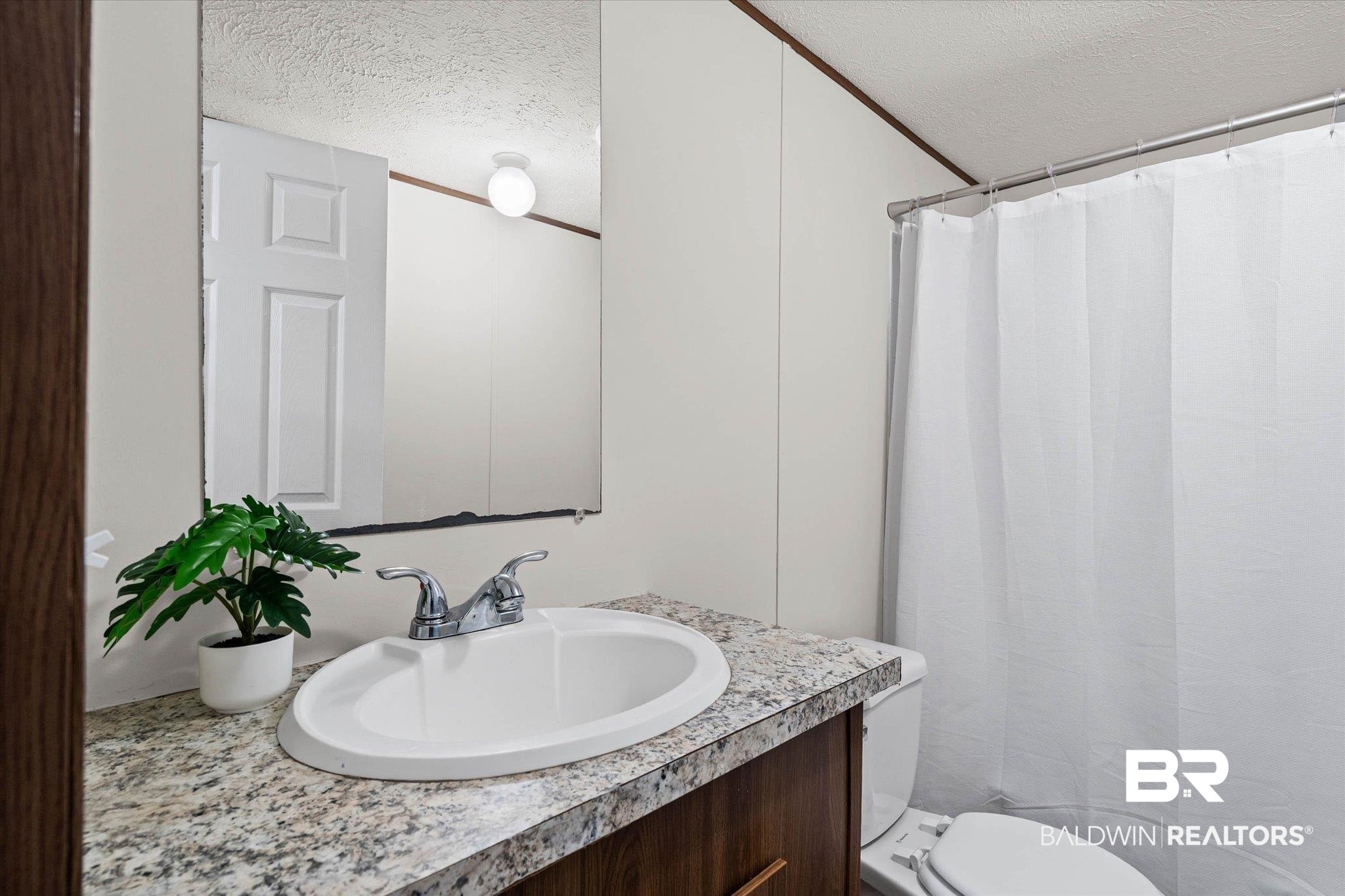 25366 Pollard Road Daphne, AL 36526 - Photo 16 of 22 Bathroom vanity featuring a white oval sink with chrome faucet, a granite-look countertop, and a wood-finish cabinet