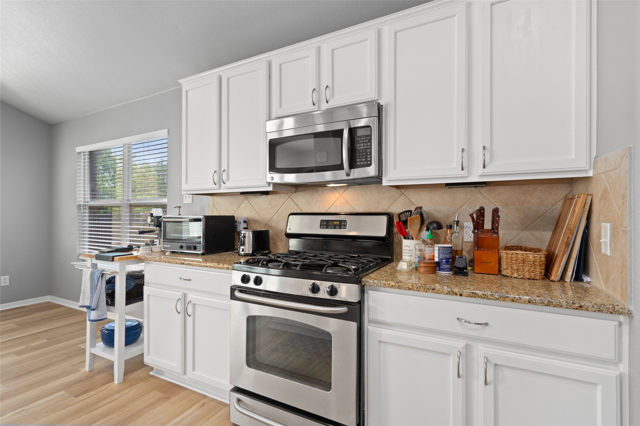 7013 Cromarty Lane Austin, TX 78754 - Photo 18 of 37 The kitchen features white cabinetry, granite countertops, a tile backsplash, and stainless steel appliances including a range and microwave