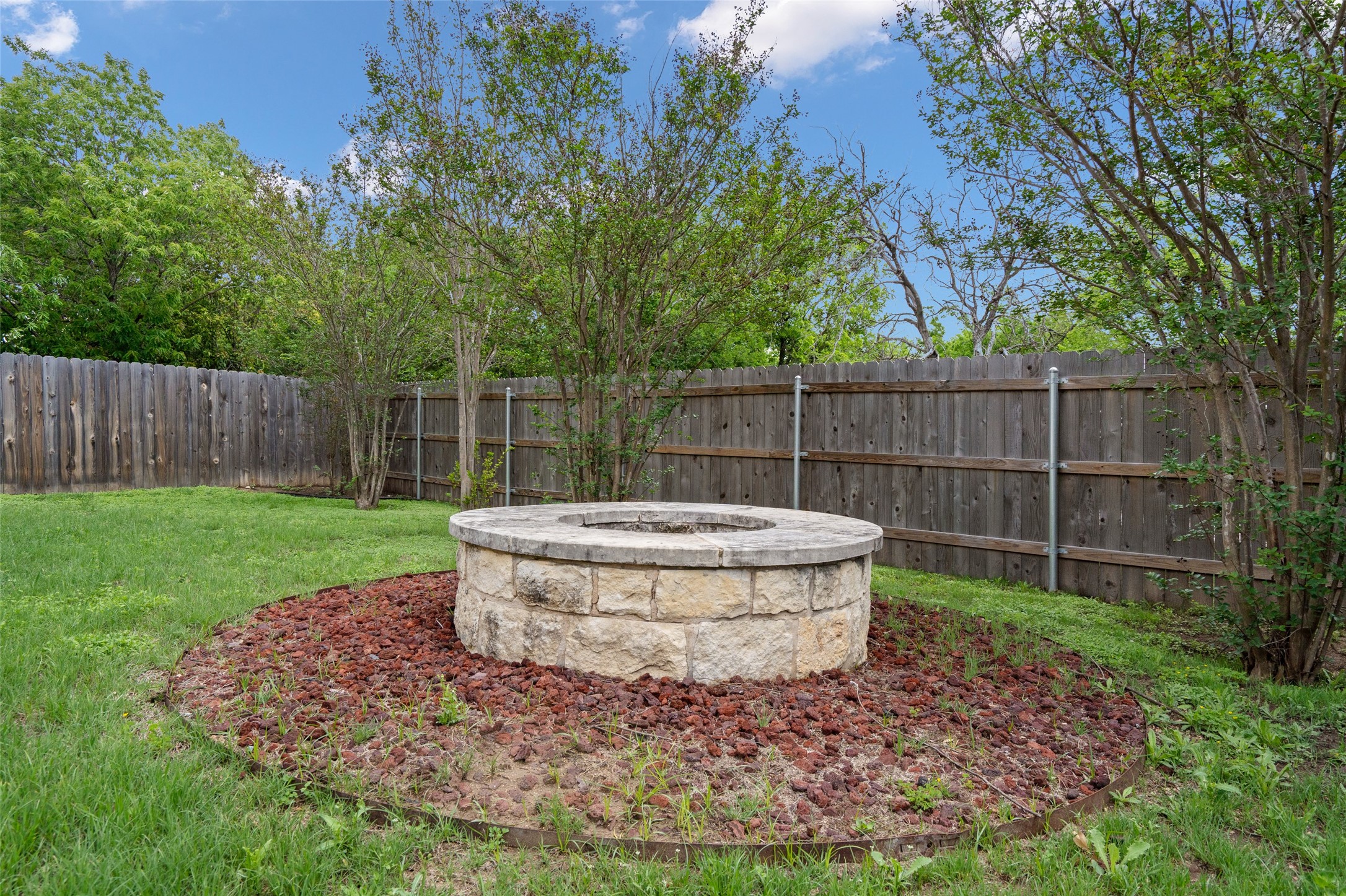 7013 Cromarty Lane Austin, TX 78754 - Photo 35 of 37 The property offers an inviting outdoor space with a stone fire pit feature, surrounded by decorative red rock and a lush green lawn