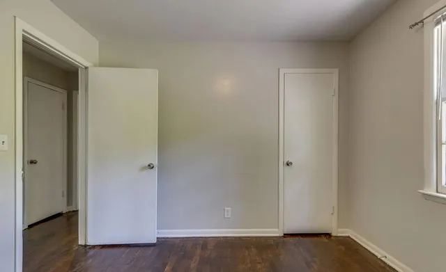 an empty room with wooden floor closet and windows